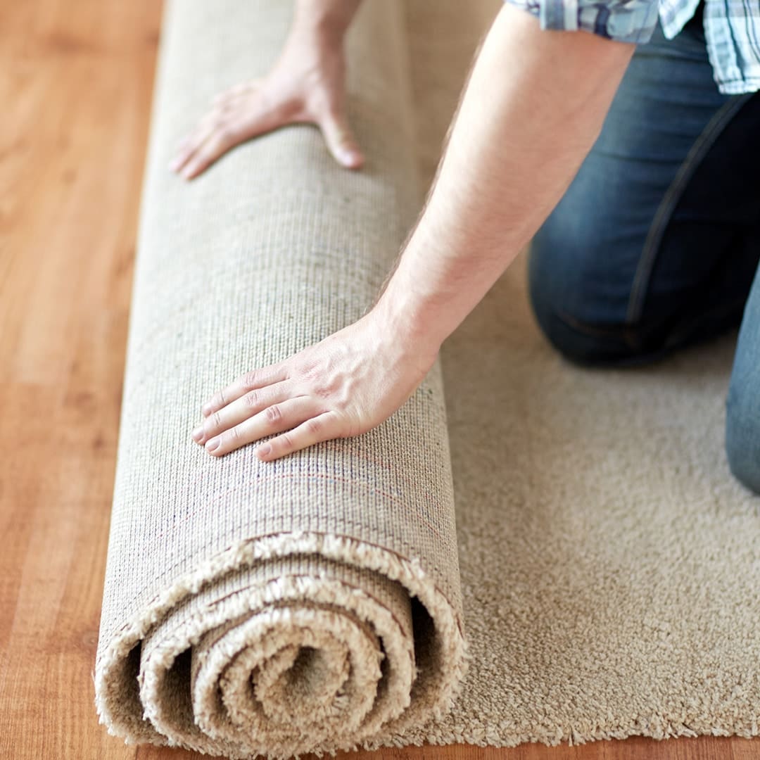 A person rolling out a cream colored carpet